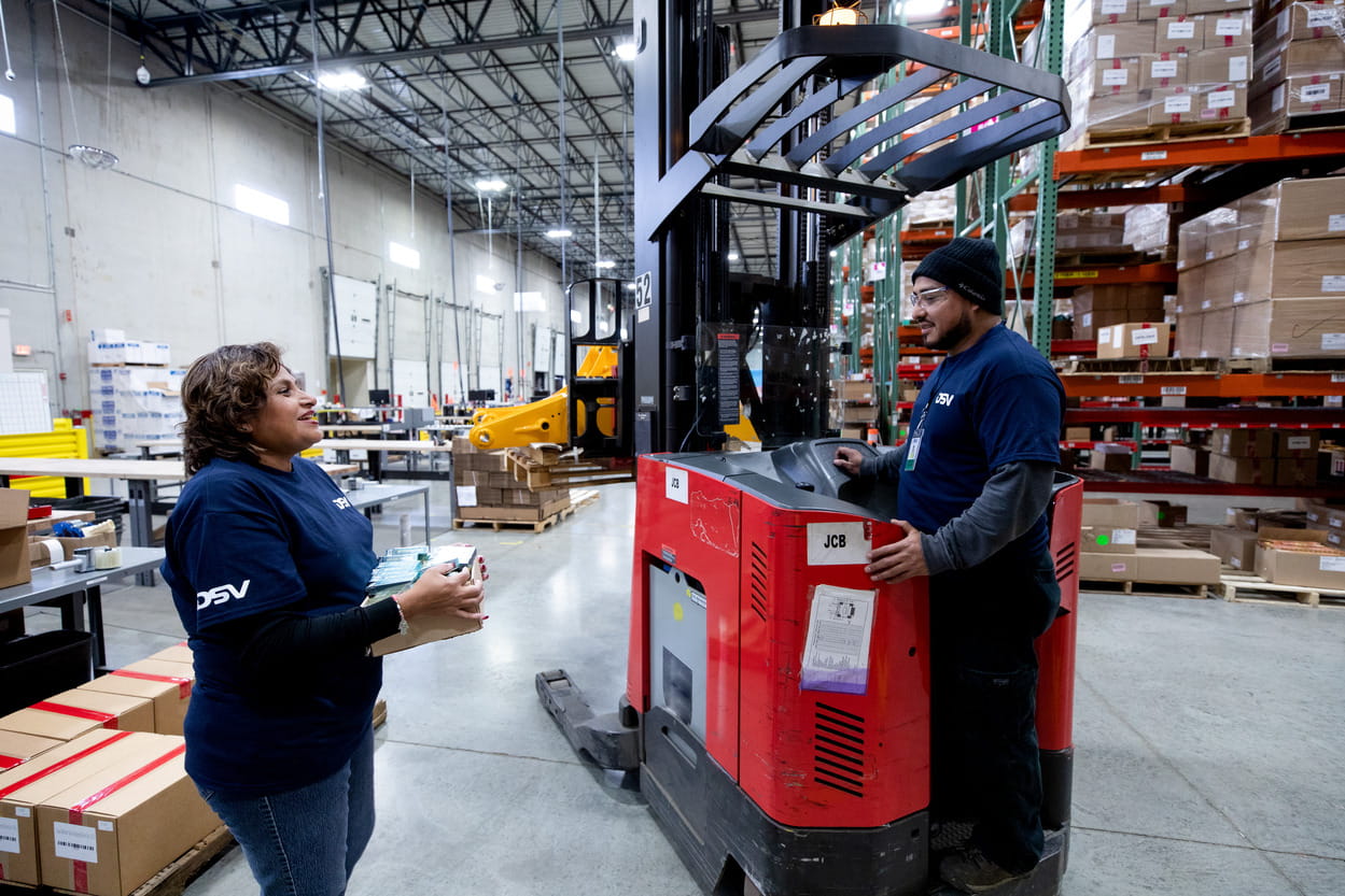 DSV-medarbeider holder på en pakke, mens den andre kjører truck på et lager.